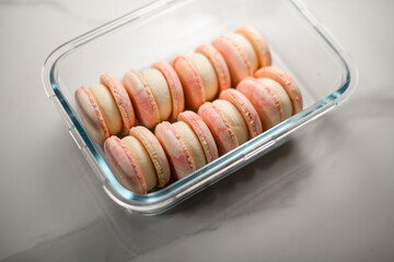 Pink macaroons with white cream neatly stacked in a rectangular transparent container