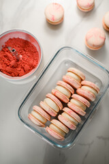 Top view of pink macaroons with white cream neatly stacked in a rectangular glass container