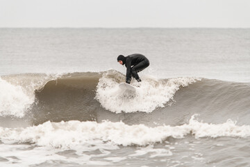 Male surfer in a black wetsuit stands on a surfboard, climbing to the top of a wave