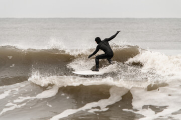 Male surfer in black wetsuit spreads his arms out to the sides for balance while standing on a surfboard