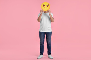 Man covering face with smiling emoticon on pink background © New Africa