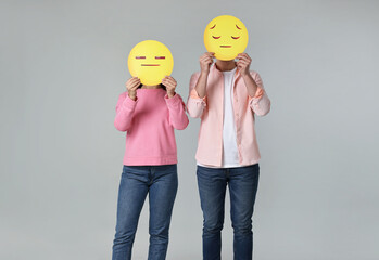People covering faces with sad emoticons on grey background