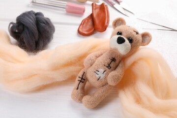 Felted bear, wool and tools on white wooden table, closeup