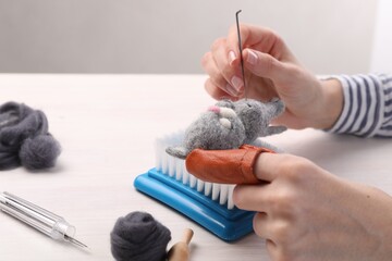 Woman felting toy cat from wool at light wooden table, closeup