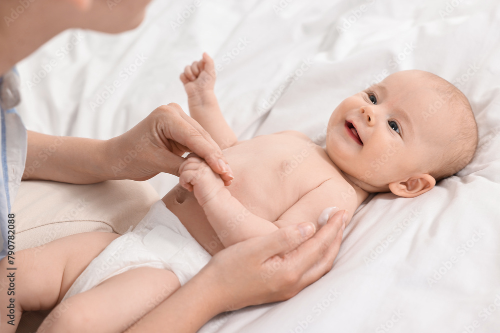 Sticker Woman applying body cream onto baby`s skin on bed, closeup