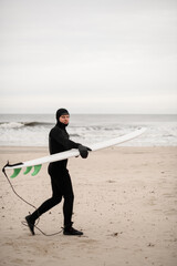 Male surfer walks along the sandy seashore with his surfboard in his hands - 790783209