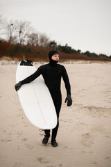 Male surfer walking on the sandy beach with his surfboard in his hands