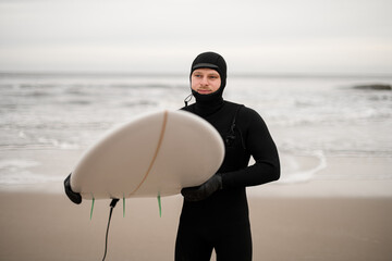 Male surfer standing on the sandy seashore with a white surfboard in his hand