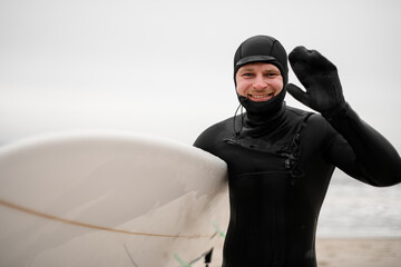 Happy smiling male surfer standing on seashore in wet clothes, water drops on face