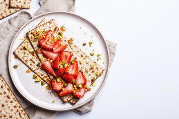 Matza toast with peanut butter, strawberries and pistachios on a white plate. Traditional bread for...