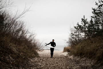 Happy male surfer walks away from the sea on a sandy path