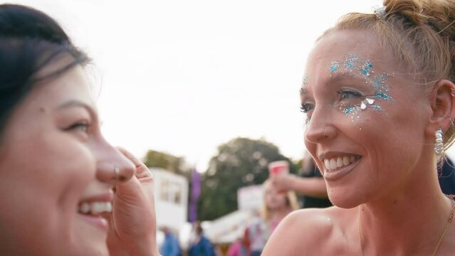 Close up of young woman having face decorated with glitter at outdoor summer music festival - shot in slow motion