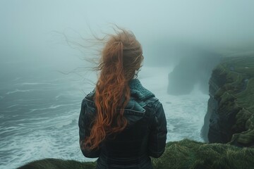 A pensive red-haired woman in a leather jacket looks out at foggy cliffs and tumultuous ocean