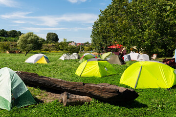 A vibrant campsite with colorful tents scattered across a lush green field, under a clear blue sky.