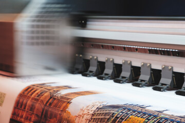 A printer is printing a picture of a city. The printer is black and silver. The image is blurry