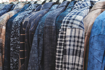 A row of plaid and checkered jackets hang on a rack. The jackets are of different colors and patterns, and they are all neatly hung up. Concept of organization and order
