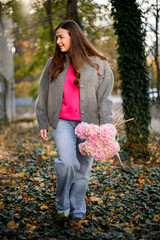 Young smiling pretty woman with a bouquet of pink hydrangeas walking on the sidewalk among fallen leaves