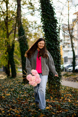 Young smiling pretty woman with a bouquet of pink large-leaved hydrangeas is walking down the sidewalk