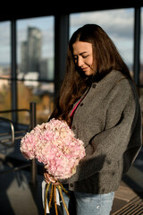 Cute smiling woman is admiring a bouquet of pink hydrangeas