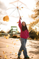 Cute smiling young woman holding an umbrella high above her head, yellow leaves swirling around her
