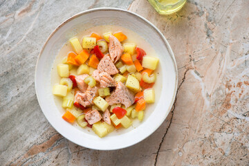 Plate of salmon and vegetable soup on a roseate granite background, horizontal shot, view from above