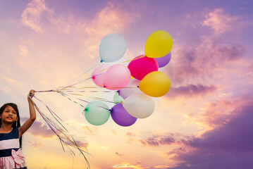 Cheerful cute girl holding balloons running on green meadow violet purple pastel sky happiness. Hands holding vibrant air balloons play on birthday party happy times summer on pueple sky outdoor
