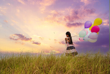 Cheerful cute girl holding balloons running on green meadow violet purple pastel sky happiness. Hands holding vibrant air balloons play on birthday party happy times summer on pueple sky outdoor