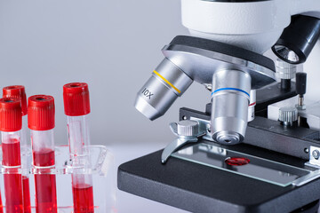 A microscope with a slide containing red blood cells. Microscope is on a laboratory table next to a few red blood cell tubes. - 790808052