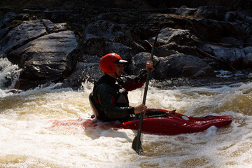 Person wearing helmet paddling red kayak along river