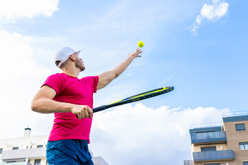 A man in a red shirt is playing tennis with a yellow ball