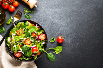 Green Salad with salad leaves and vegetables at black background. Flat lay with copy space.