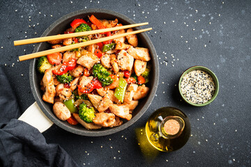 Stir fry chicken and vegetables and sesame at black background. Asian cuisine. Top view with space for design.
