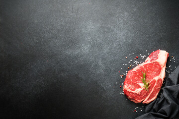 Raw meat steak with spices on black background. Beef steak ribeye. Top view with copy space.