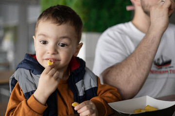 A child with a funny facial expression is eating french fries. An emotional child enjoys life. Happy childhood.