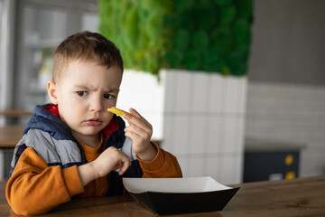A child with a funny facial expression is eating french fries. An emotional child enjoys life. Happy childhood.