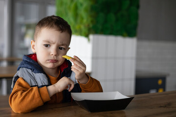 A child with a funny facial expression is eating french fries. An emotional child enjoys life....