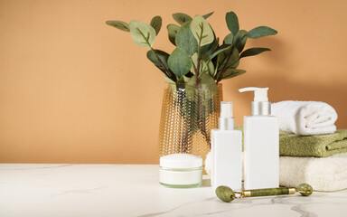 Skin care products in the bathroom. Face cream, serum bottle, jade roller and stack of towels. - 790812499