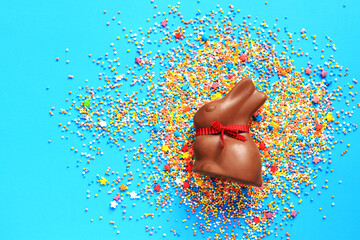 Chocolate bunny and colored sugar sprinkles on a blue background, top view. Easter composition....