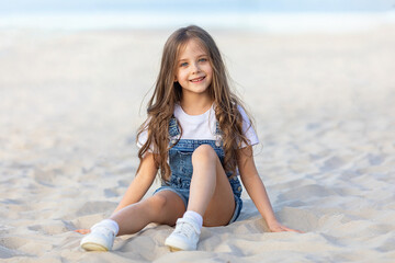 Happy little girl playing and has fun on a white sandy beach near the ocean in summer. Children's...