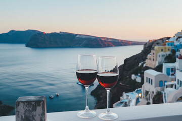 two glasses of red wine on the terrace in a greek town, beautiful sunset over the ocean or sea, summer vacation or holiday