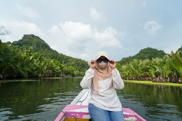 Portrait of woman sitting in wooden boat. Asian woman wearing a hijab sits on a wooden boat that is...