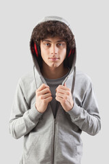 Handsome young man wears headphones and a hoodie sweatshirt and is isolated against a gray background. He looks into the camera with his blue eyes while listening to music