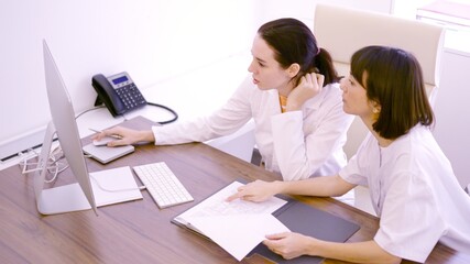 Colleagues discussing about medical report using computer in the clinic