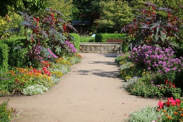 sandy path in a flower park and at the end of the path there is a brick fountain