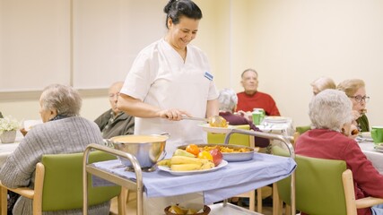Friendly cook serving food to seniors in nursing home