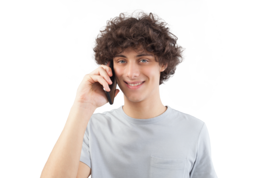 A young, handsome man smiles as he uses his smartphone, talking and listening with cellphone while looking into the camera with his blue eyes. He is isolated against a white background