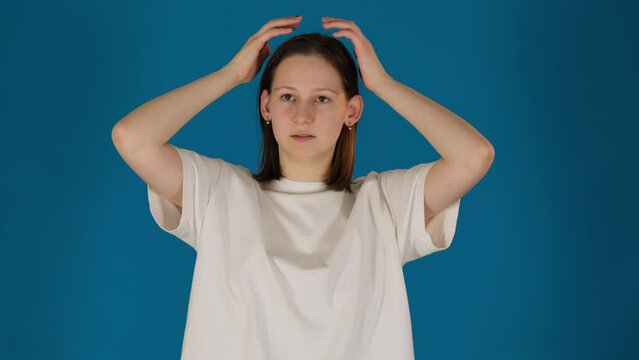 Lady adjusts hair with appearance in mind on blue background. Woman examines reflection with gaze scrutinizing every strand with eye for perfection slow motion