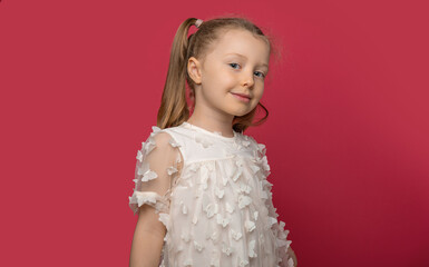Little cheerful girl in a light dress on a pink background.