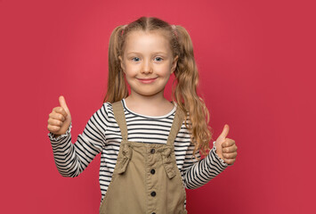 Little cheerful girl shows thumbs up on a pink background.