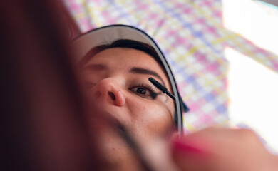 Latin woman applying mascara in front of mirror in low angle shot